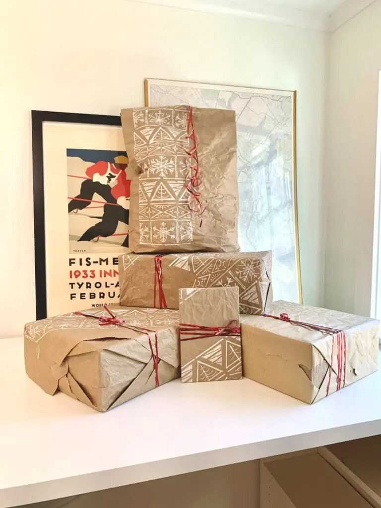 A stack of brown paper-wrapped gifts with a white Christmas pattern stenciled on them