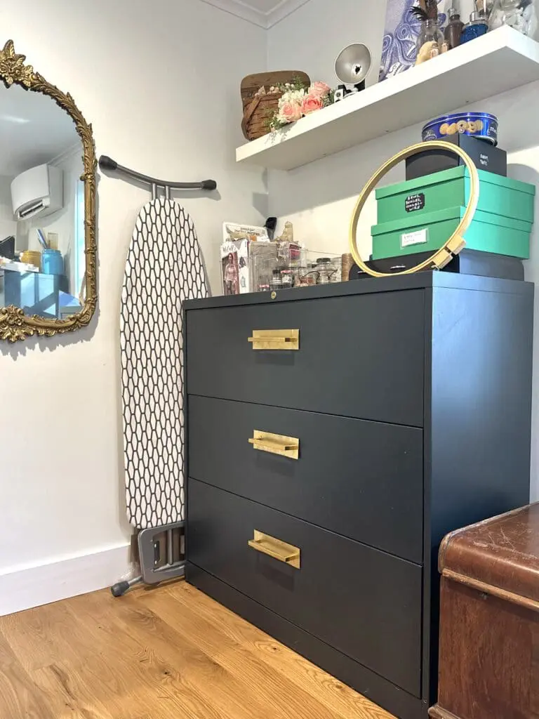 Dark green cabinet with gold handles with craft supplies stored on top of it