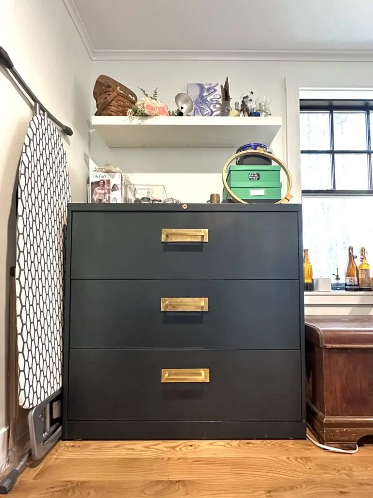 Dark green cabinet with gold handles with craft supplies stored on top of it