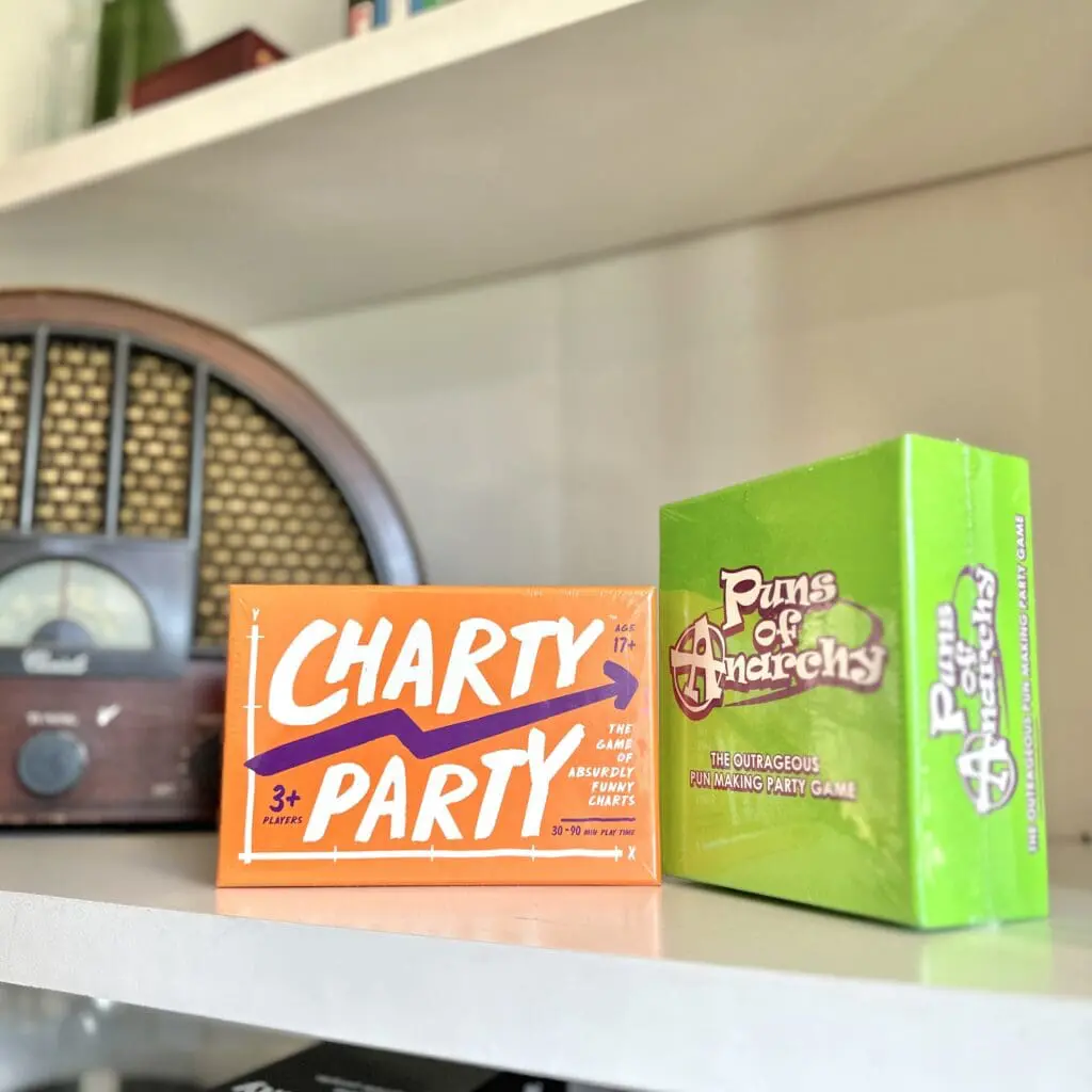 Two card game boxes, Charty Party and Puns of Anarchy, sitting on a bookshelf